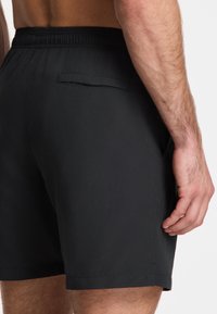 Schwarze Badehosen mit einem elastischen Bund und einer Gesäßtasche, aus glattem Stoff und mit einem schlichten Design, über dem Knie geschnitten.