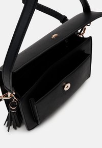 Černá kožená kabelka se strukturovaným tvarem, vybavená magnetickým zapínáním, vnitřní kapsou a ozdobným třásňovým detailem.