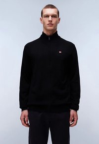 Black zip-up sweater with a high collar, knitted texture, and a small red and white logo on the left chest. Worn by a male model.