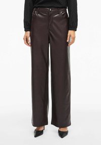 Pantalons larges en simili cuir marron avec poches avant, fermeture à bouton et texture lisse. Assortis avec des talons noirs pointus.