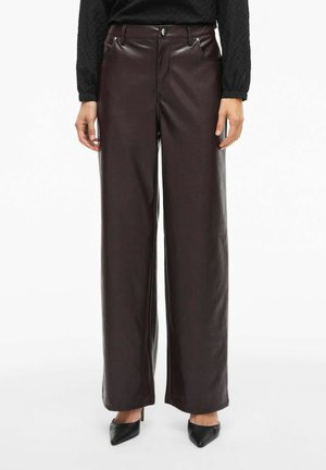 Braune Kunstleder-Hosen mit weitem Bein, Fronttaschen, Knopfverschluss und glatter Textur. Kombiniert mit spitzen schwarzen Absätzen.