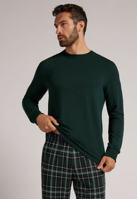 Ciemnozielona koszula z długim rękawem i okrągłym dekoltem, w połączeniu z dresowymi spodniami w kratę w kolorze czarnym i zielonym, z elastycznym pasem.