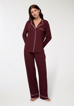 Completo pigiama bordeaux in tessuto morbido, con una camicia con bottoni e tasca, rifinita con piping bianco, abbinata a pantaloni larghi.
