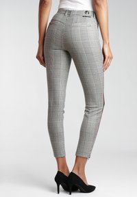 Svartvita rutiga byxor med en åtsittande design, ankellängd och en kontrasterande röd sidosträv, i kombination med svarta högklackade skor.