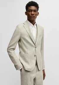 Licht beige pak met gestructureerde stof, enkelgeknoopte ontwerp, twee zakken, grijze knoop, gecombineerd met een witte overhemd met kraag eronder.