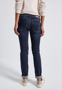 Tight-fit mörkblå jeans av denim, med fem fickor, bakstycke och uppvikta fållar. Minimalistisk design utan synlig logotyp.