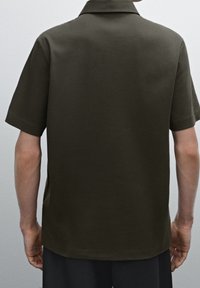 Chemise à manches courtes vert olive avec un col plat, une texture lisse, un ourlet droit, sans motifs ni ornements visibles.