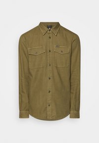 Oliivinvihreä, nappikiinnitteinen paita, valmistettu teksturoidusta kankaasta, jossa on kaksi rintataskua, kaulus ja kaartuva helma. Korostettu mustilla napeilla.