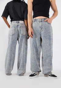 Jeans in denim blu chiaro oversize con taglio dritto, caratterizzati da un lavaggio sbiadito e dal classico design a cinque tasche. Indossati con sneakers casual.