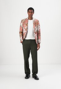 Blazer mit Blumenmuster in Pink-, Orange- und Grüntönen, kombiniert mit einem weißen T-Shirt und olivgrünen Hosen. Schwarze Schuhe vervollständigen den Look.