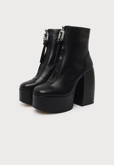 Paire de bottines noires en cuir à plateforme avec talons hauts épais, fermetures éclair à l'avant et ferrures métalliques décoratives avec languettes de tirage.