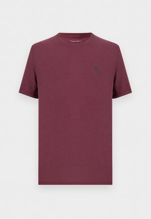 Egyszínű bordó rövid ujjú, kerek nyakú póló kis sötét emblémával a bal mellkason, a Pier One-tól.