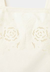 Tissu blanc avec découpes florales complexes et motifs de roses brodées près du bord supérieur.