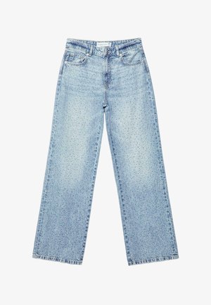 Jean taille haute bleu clair porté par une personne, vu de dos, avec des jambes larges et deux poches arrière. Bracelets noirs et bleu marine au poignet droit.