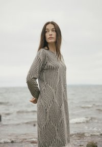 Langärmeliges Strickkleid in Beige mit schwarzen Wellenmustern. Es hat einen runden Halsausschnitt und ist so gestaltet, dass es knapp über dem Knie endet.