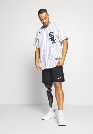 Tricou de baseball alb pentru bărbați cu dungi negre și logo, asociat cu pantaloni scurți Nike negri și adidași sportivi albaștri, punând în evidență o picior protezic.