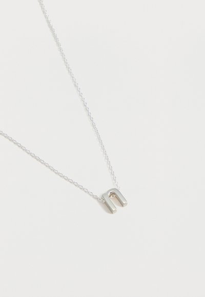 Collier en argent avec un petit pendentif en forme de fer à cheval sur une chaîne délicate sur fond blanc.
