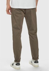 Bruna avsmalnande byxor i ett texturerat tyg, med en lätt uppvikt fåll, kombinerade med vita sneakers som har svarta och grå accenter.