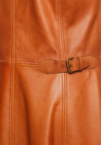 Brun läderbit med en slät yta, med ett sidbälte som har ett mässingsspänne och detaljerad sömnad längs sömmarna.