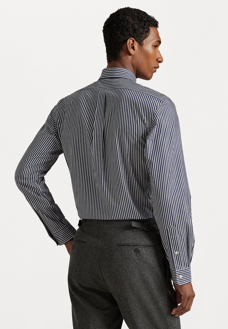 Chemise à rayures bleu marine et blanche à manches longues avec col haut et poignets à boutons, accompagnée de pantalons gris texturés avec poches arrière.