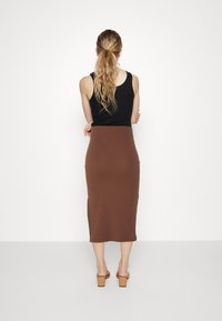 Haut noir sans manches associé à une jupe marron côtelée jusqu'aux genoux. La tenue présente une silhouette ajustée et un tissu texturé, portée avec des sandales nude.