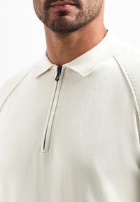 Lichtbeige pullover met een ritskraag, textuur breiwerk, en raglanmouwen, met een minimalistisch ontwerp zonder patronen.