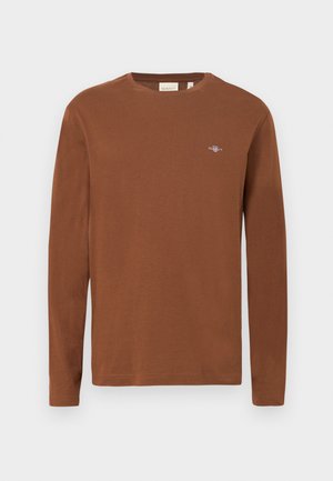 Hnědé tričko s dlouhým rukávem vyrobené z bavlny. Má kulatý výstřih a malou vyšívanou značku na hrudi. Hladká textura.