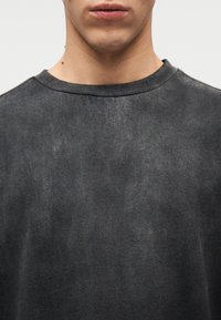 Κοντινό πλάνο του κάτω μέρους του προσώπου και του λαιμού ενός ατόμου που φοράει μια ξεθω ριασμένη μαύρη μπλούζα με στρογγυλή λαιμόκοψη και υφασμάτινη υφή.