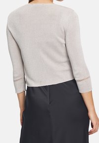 Ljust gråkort ärmad tröja med trekvartslånga ärmar, med ett strukturerat stickat mönster och spetsdetaljer vid ärmsluten.