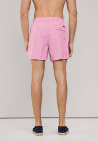 Różowe kąpielówki w wzory z elastycznym paskiem w talii i tylną kieszenią. Materiał wydaje się lekki o gładkiej fakturze.