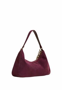 Borsetta in suede bordeaux con forma curva, tracolla singola e dettaglio in catena dorata, dotata di chiusura a zip laterale.
