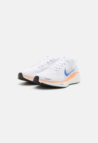 White athletic shoes with a breathable mesh upper, featuring a blue Nike swoosh, orange midsole accents, and a textured black outsole.