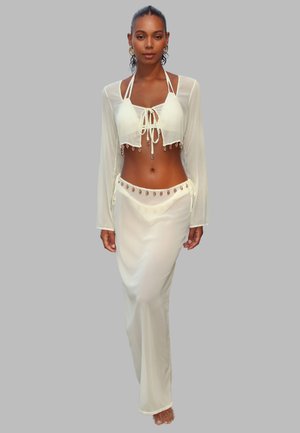 White two-piece ensemble featuring a cropped, sheer long-sleeve top with drawstring, and a long skirt adorned with decorative accents.