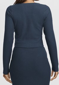 Marineblaue Rippstrick-Langarmbluse mit Rundhalsausschnitt und figurbetontem Design, das einen strukturierten Stoff und eine verkürzte Länge auf Taillenhöhe hervorhebt.