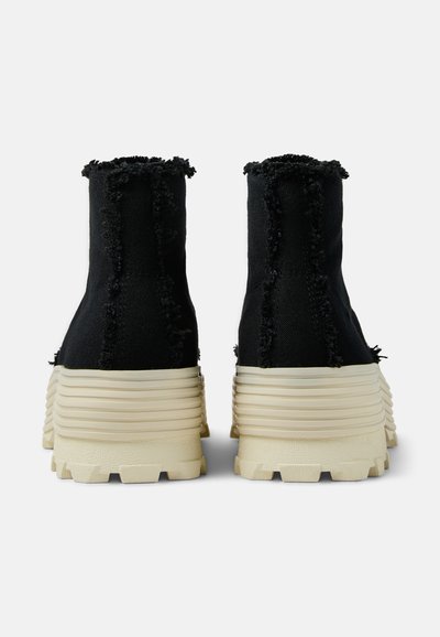 Sneakers alte nere realizzate in tessuto testurizzato con bordi sfilacciati, dotate di una suola rigata di un off-white e un design a trazione massiccia.
