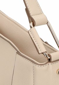 Beige Handtasche aus Leder mit glatter Textur, flacher Form, goldenen Hardware-Akzenten und verstärkten Nähten entlang der Kanten.