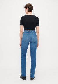 Korkeavyötyiset siniset farkut suoranlahkeisella muotoilulla, joissa on kaksi takataskua ja sileä pinta. Musta istuva t-paita päällä.