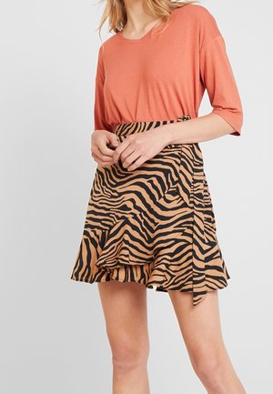 Top color ruggine con maniche corte abbinato a una gonna beige con stampa a zebra nera e orlo arricciato.