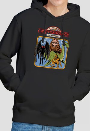 Black hoodie featuring colorful illustrations of cryptids including Mothman, Bigfoot, Loch Ness Monster, and a small dinosaur under "Cryptozoology for Beginners" text.