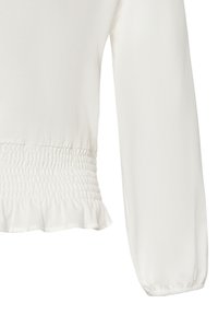 Weiße Bluse mit gestuftem Taillengummi, langen Ärmeln mit elastischen Bündchen und einem volantrundem Saum. Der Stoff wirkt leicht und glatt.
