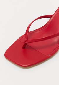Røde flate sandaler laget av glatt lær, med en smal tårem og firkantet tådesign. Sålen er flat og diskret.