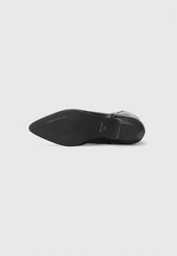 Ballerine en cuir noir avec un bout pointu, texture lisse et un talon slim légèrement effilé. Présente le logo de la marque sur la semelle.