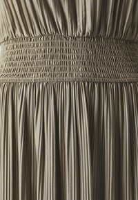 Smocked waist dress featuring soft, pleated fabric in a muted beige tone. The texture is smooth with subtle vertical stripes.