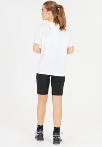 Vit kortärmad t-shirt kombinerad med svarta knäl�ånga shorts med en enkel design. Bärs med grå och blå vandringsskor.