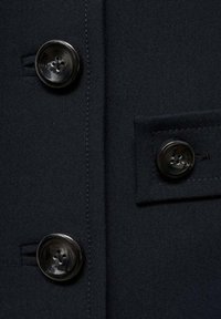 Navy fabric coat section featuring large, round, glossy black buttons and a side pocket with neatly stitched edges.