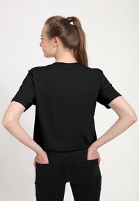 T-shirt in cotone nero con maniche corte, collo rotondo e vestibilità rilassata, visto da dietro. Abbinato a jeans neri.