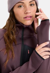 Getailleerde, gestructureerde zip-up jack in diep paars met zwarte accenten. Heeft een hoge kraag, duimgaten en een roze ritslip voor extra detail.