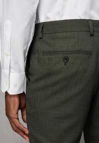 Mørkegrønne teksturerede bukser med en slim fit, der har en baglomme med en sort knap, parret med en hvid skjorte med knapmanchetter.