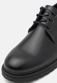 Chaussure en cuir noir à texture lisse, bout arrondi et design classique avec lacets. Dispose d'une semelle en caoutchouc épaisse et robuste pour une durabilité accrue.