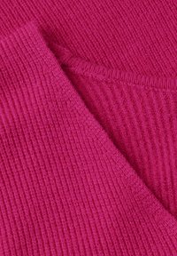 Gros plan sur un tissu tricoté côtelé rose vif avec une couture visible et une section pliée montrant la texture et les détails des coutures.